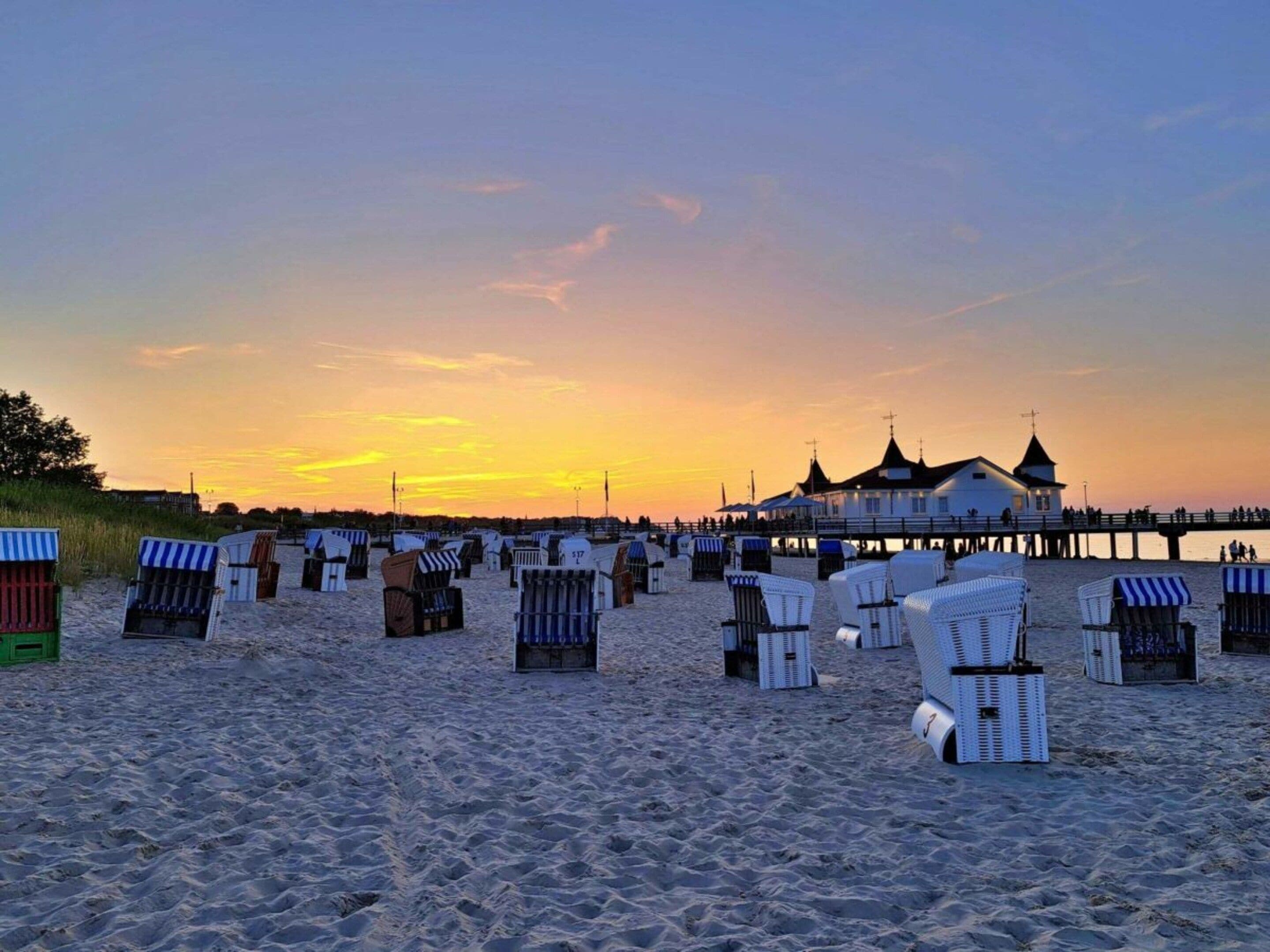 A beach with rows of beach chairs and a pier with a building at the end.