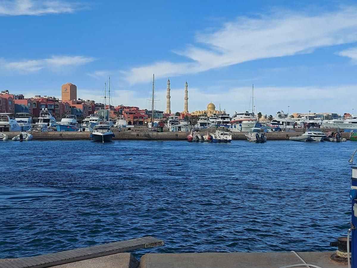 A marina with boats docked, a mosque with two minarets, and a dome in the background.