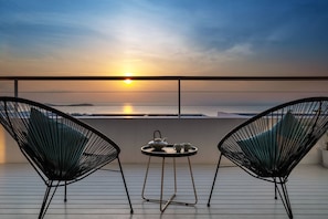 Ein Balkon mit zwei Stühlen und einem Tisch, mit Blick auf einen Sonnenuntergang über dem Meer.
