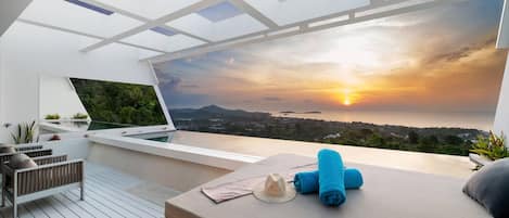A modern rooftop terrace with a laptop, seating area, and a view of the sunset over a coastal landscape.