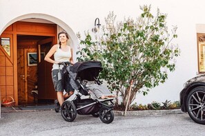 Eine Person mit einem Kinderwagen vor einem Gebäude mit einer Holztür und einem kleinen Baum.