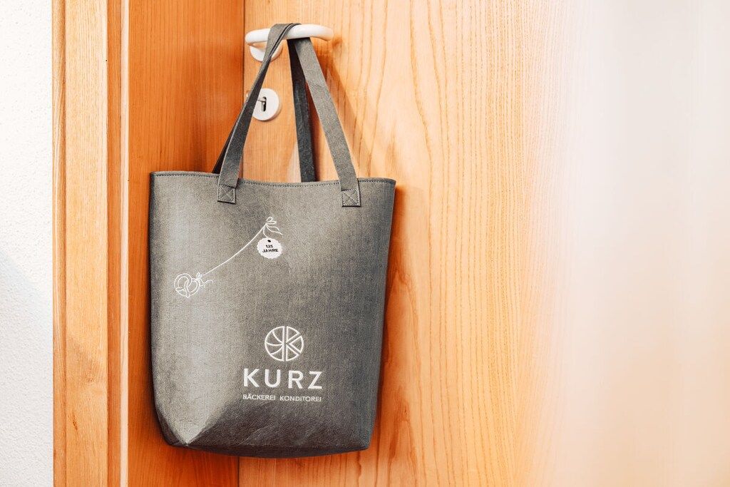 A grey tote bag hanging on a wooden door handle.