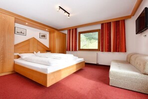 Ein Schlafzimmer mit einem hölzernen Bett, einer Couch, einem Fenster mit Vorhängen und einem Wand-Fernseher.