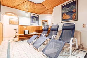 Ein Zimmer mit Holzboden und -wänden, einer Bank und vier Liegestühlen mit Netzbezügen.