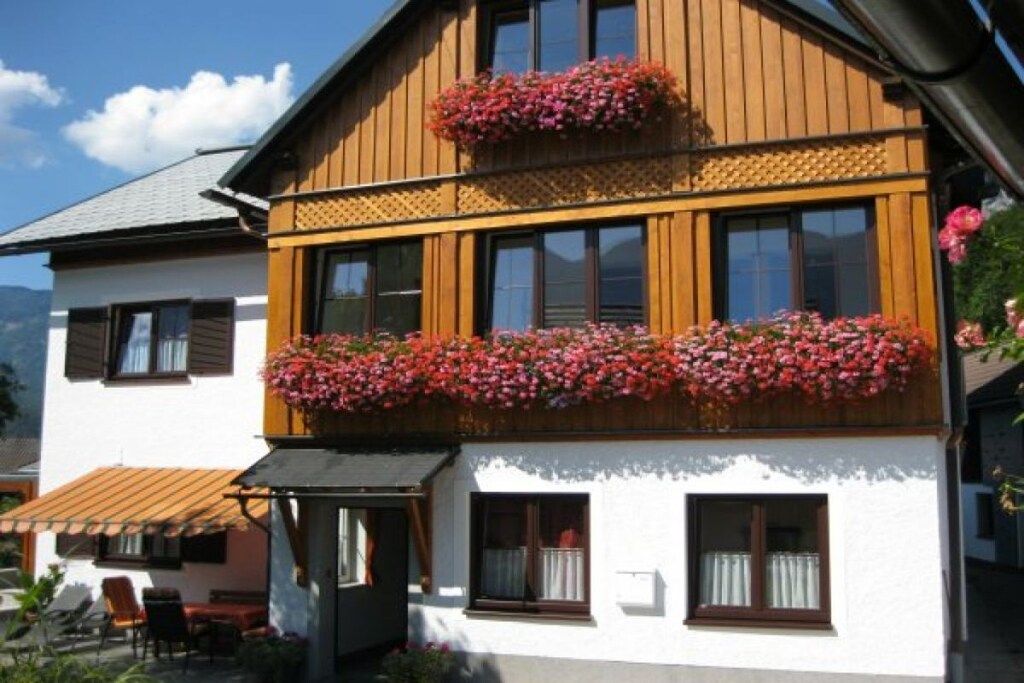 Un edificio de dos pisos con un balcón decorado con flores, fachada de madera y exterior blanco.