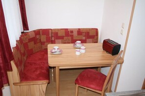 A compact room with a wooden table, a red cushioned bench, a red toaster, and a white wall. - Musler on the ground floor (Bad Goisern am Hallstättersee)
