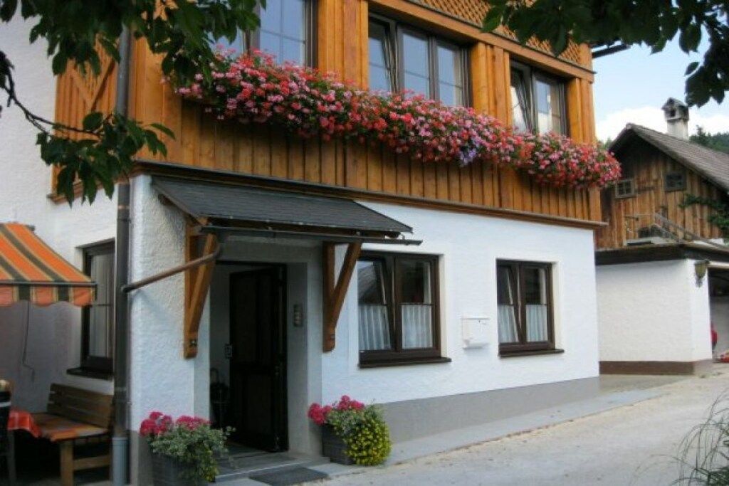 Een wit gebouw met een houten balkon versierd met bloemen, een overdekte ingang en een zichtbaar raam.