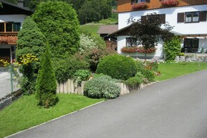 A residential area with a white house, a paved driveway, and various greenery including trees and shrubs. - Musler on the ground floor (Bad Goisern am Hallstättersee)