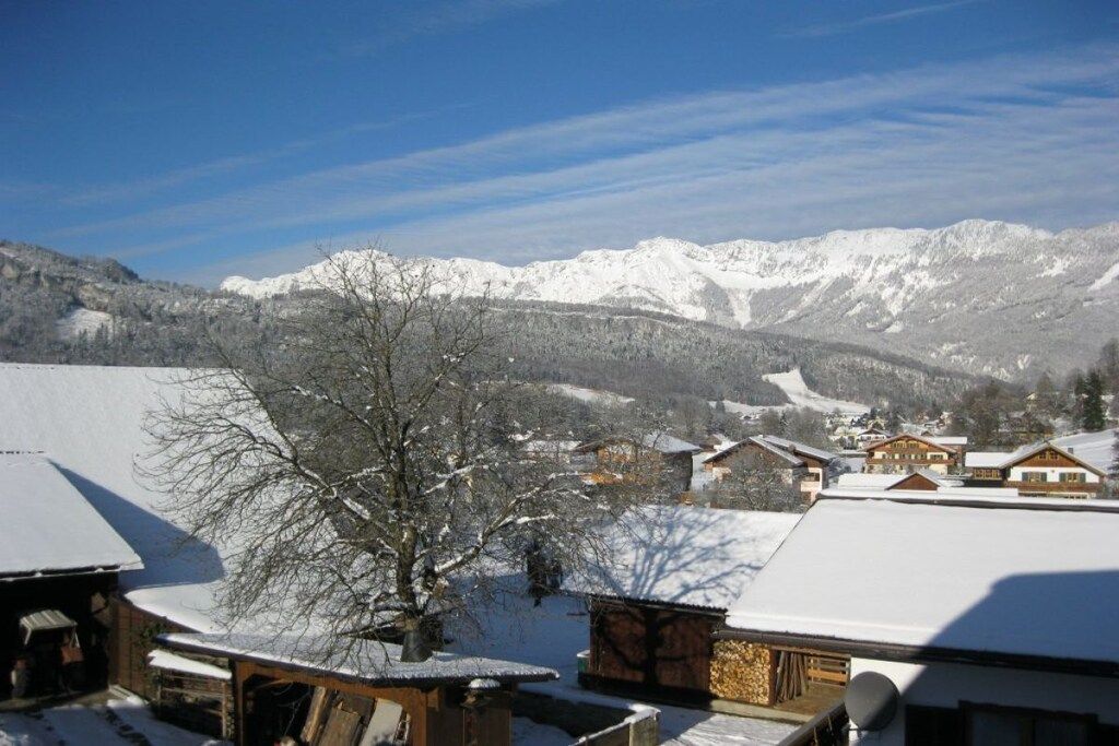Ein verschneites Dorf mit traditionellen Holzhäusern, klarem Himmel und Bergen im Hintergrund.