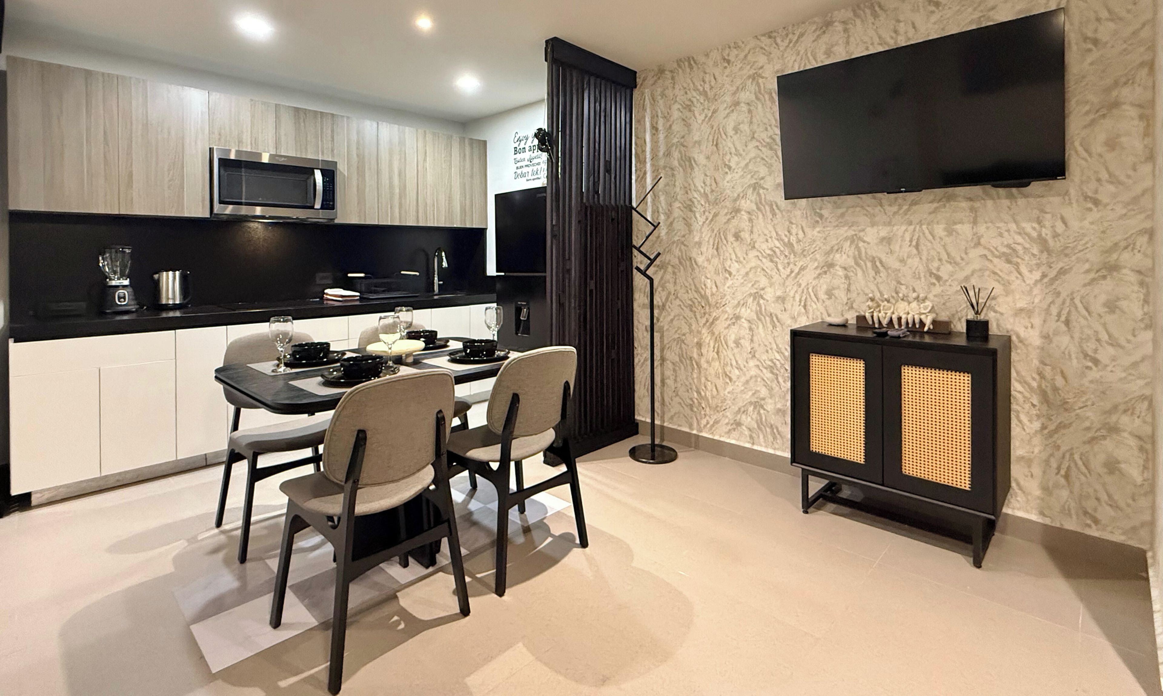 A modern kitchen with a dining area, a flat-screen TV mounted on the wall, and a black cabinet with decorative items.