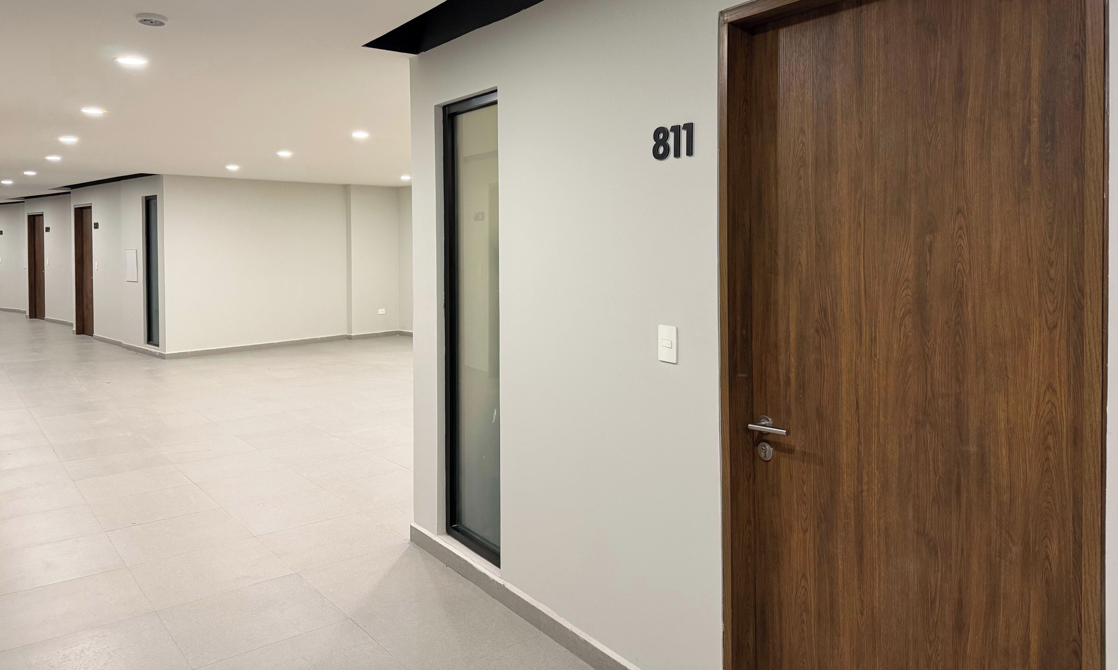 A hallway with a wooden door marked with the number 811, a glass door, and a light switch on the wall.