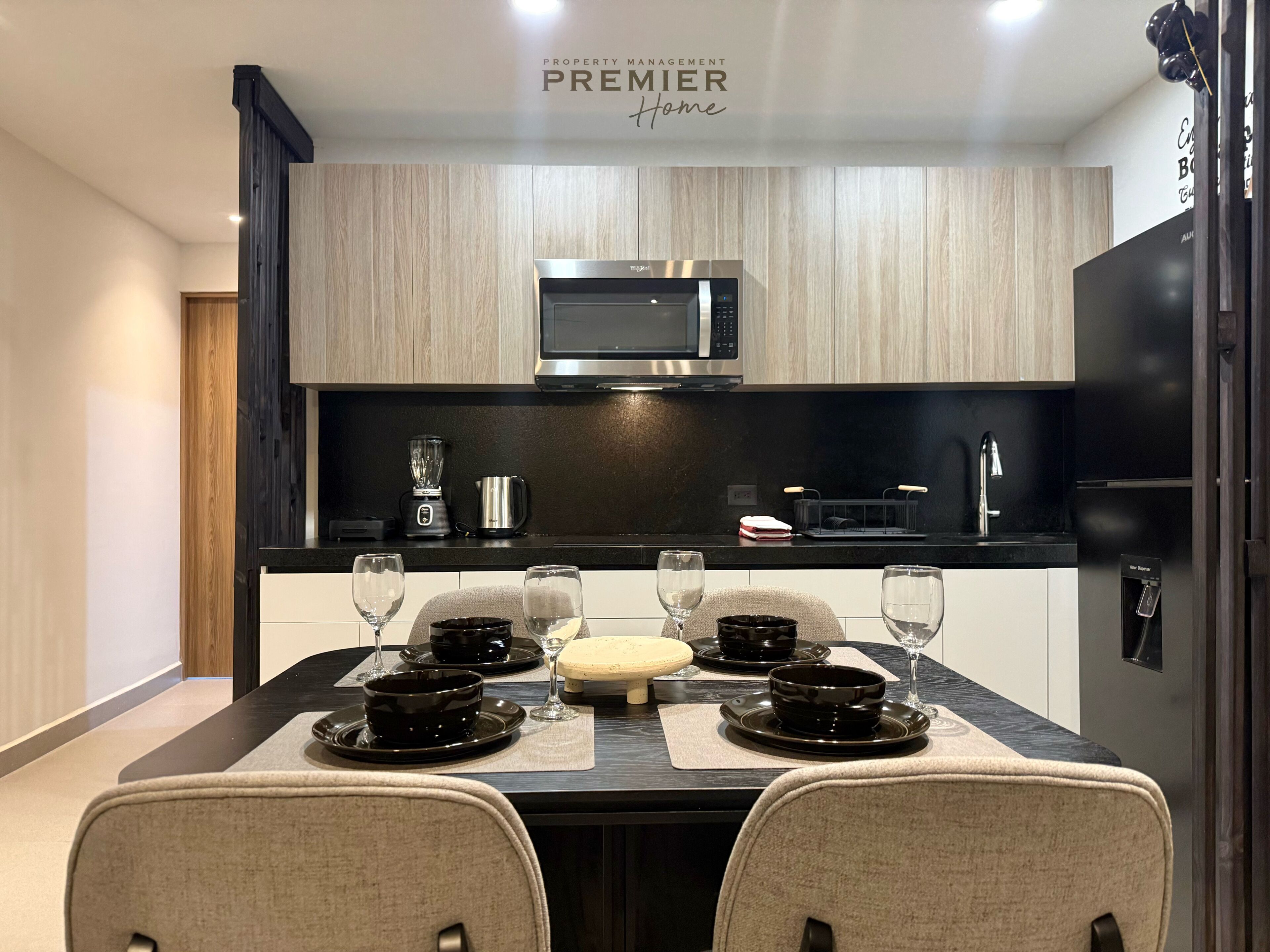 Een moderne keuken met een eettafel voor vier personen, voorzien van een magnetron, koffiezetapparaat en zwarte keukenkastjes.