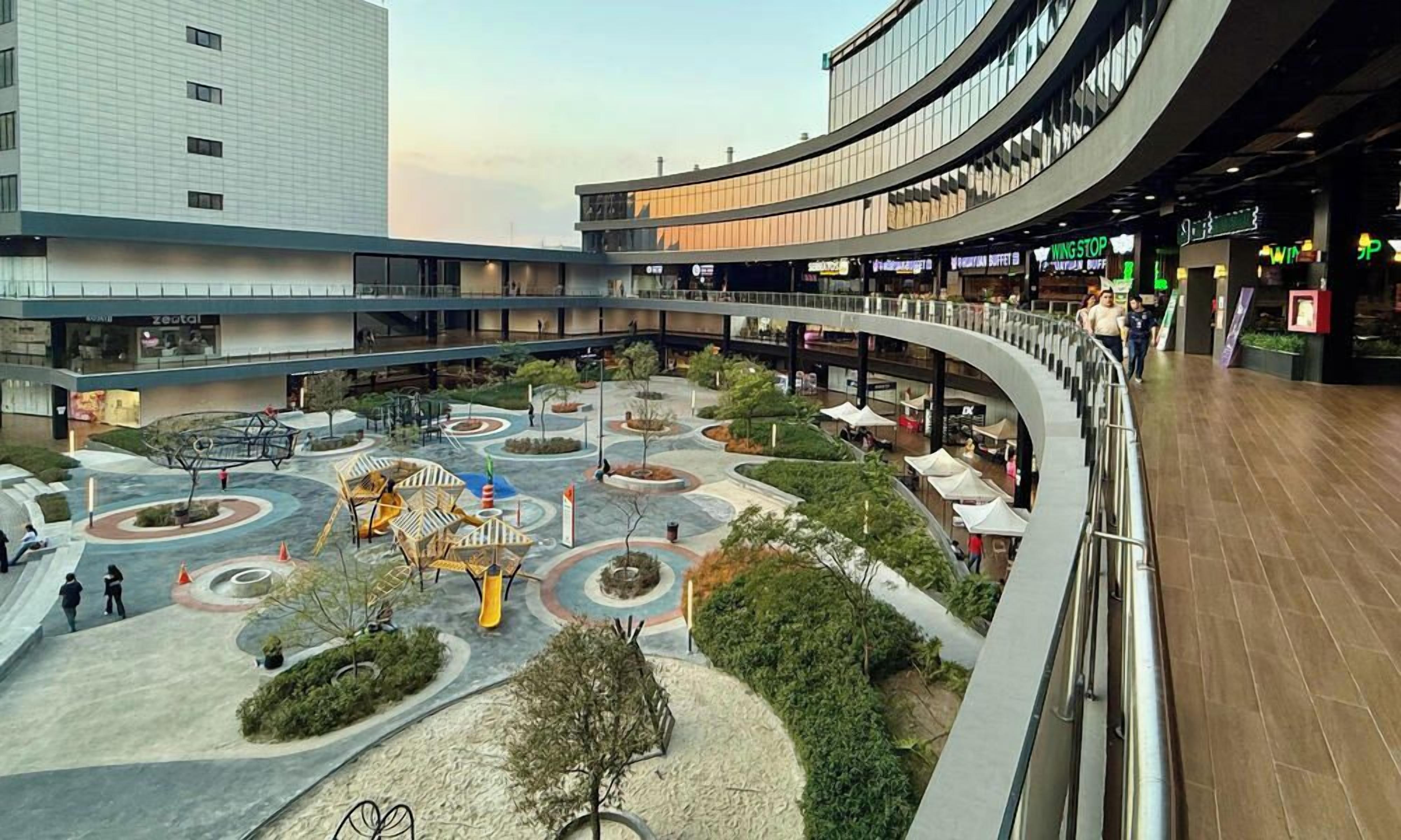 A multi-level shopping mall with a central courtyard, escalators, and various retail stores.
