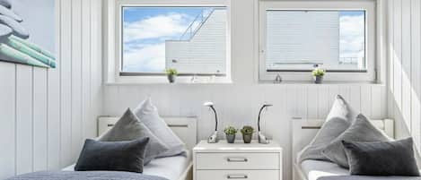 Une chambre avec deux lits, une table de chevet avec des lampes et des fenêtres donnant sur des immeubles.