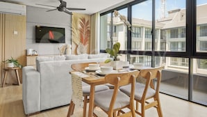 A modern living room with a sofa, dining table, chairs, and a TV mounted on the wall. - Galia by Kozystay - Nusa Dua (South Kuta)