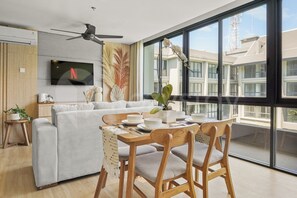 Una sala de estar moderna con sofá, mesa de comedor, sillas y un televisor montado en la pared.