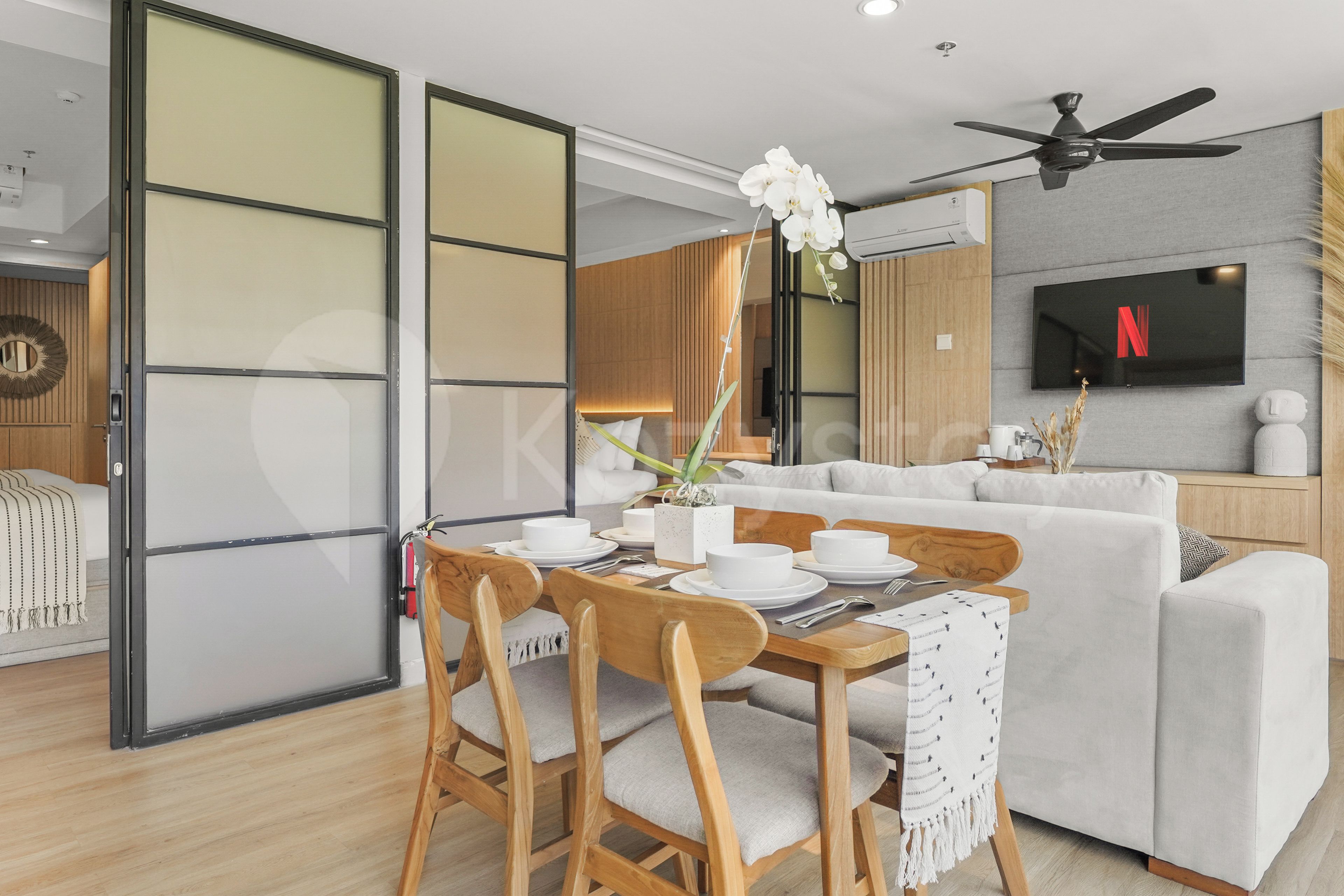 A modern living room with a dining area, a sofa set, a flat-screen TV, and a ceiling fan.