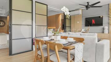 A modern living room with a dining area, a sofa set, a flat-screen TV, and a ceiling fan.