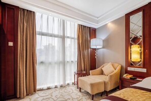 Habitación de hotel con un ventanal grande, un sofá, una mesita de noche y una lámpara.