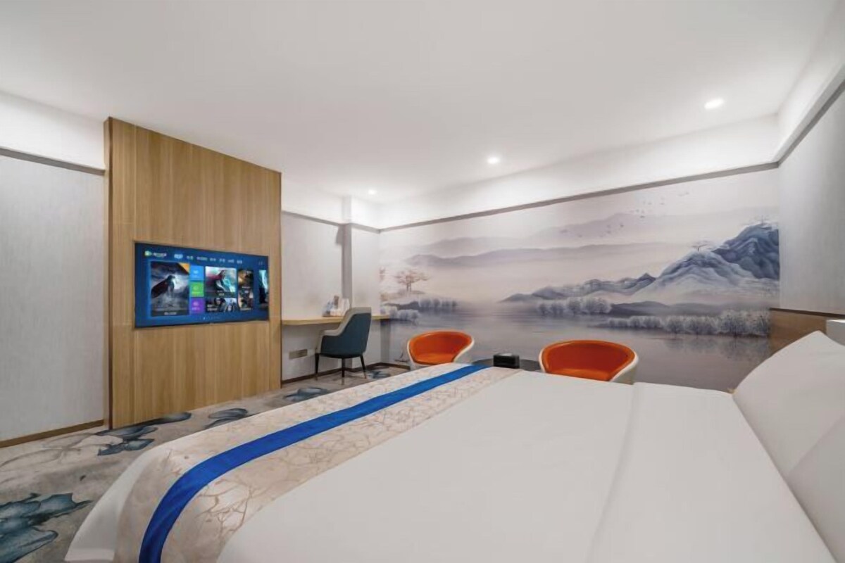 Habitación de hotel con una cama grande, un escritorio, dos sillas, un televisor y un mural en la pared.
