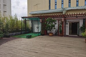 Un patio con terraza de madera, zona de estar cubierta y acceso a un edificio.