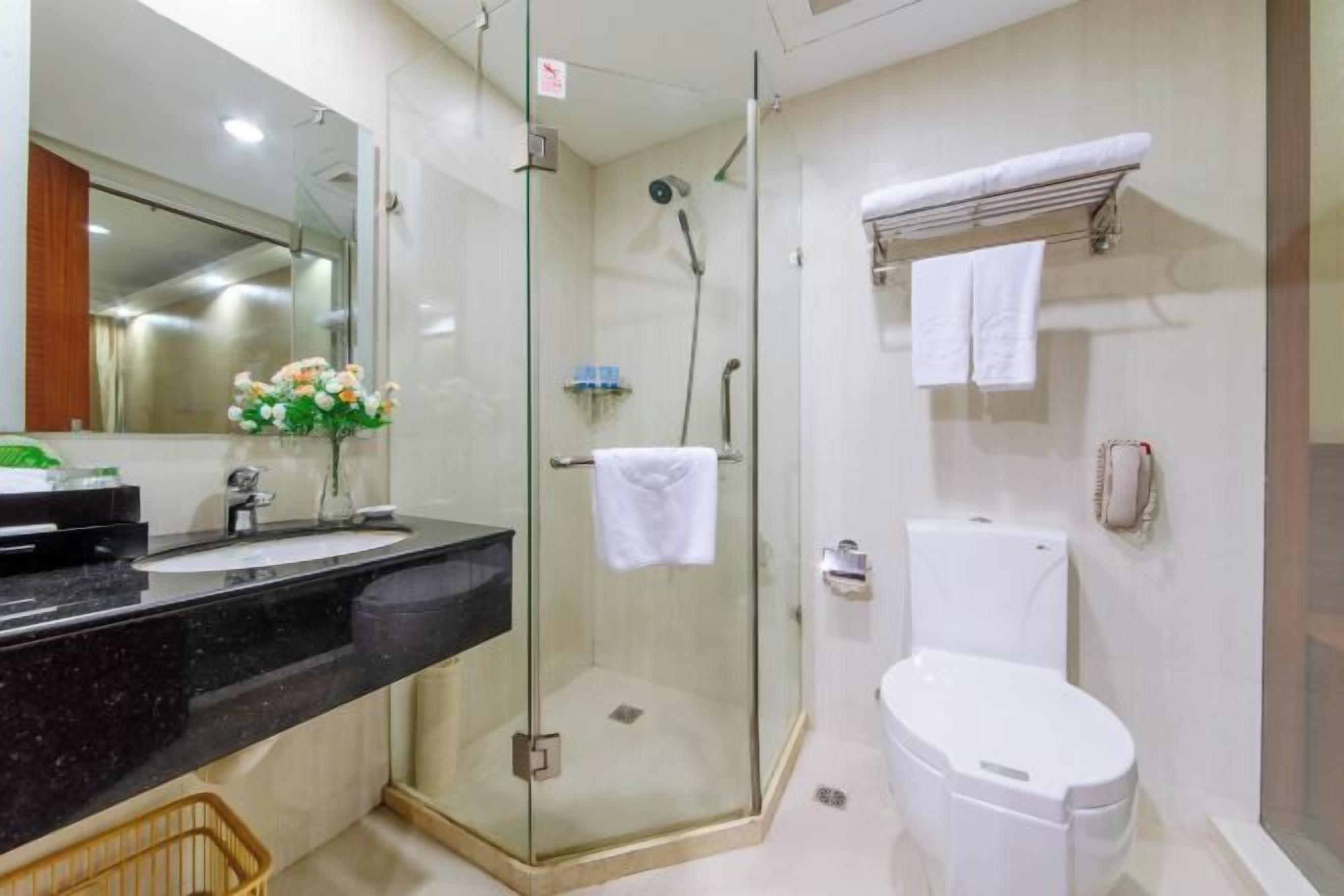 Un bagno moderno con doccia vetrata, un water bianco e un piano lavabo nero con lavandino.