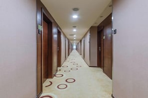 Un pasillo de hotel con puertas a ambos lados, una alfombra con diseños circulares e iluminación en el techo.