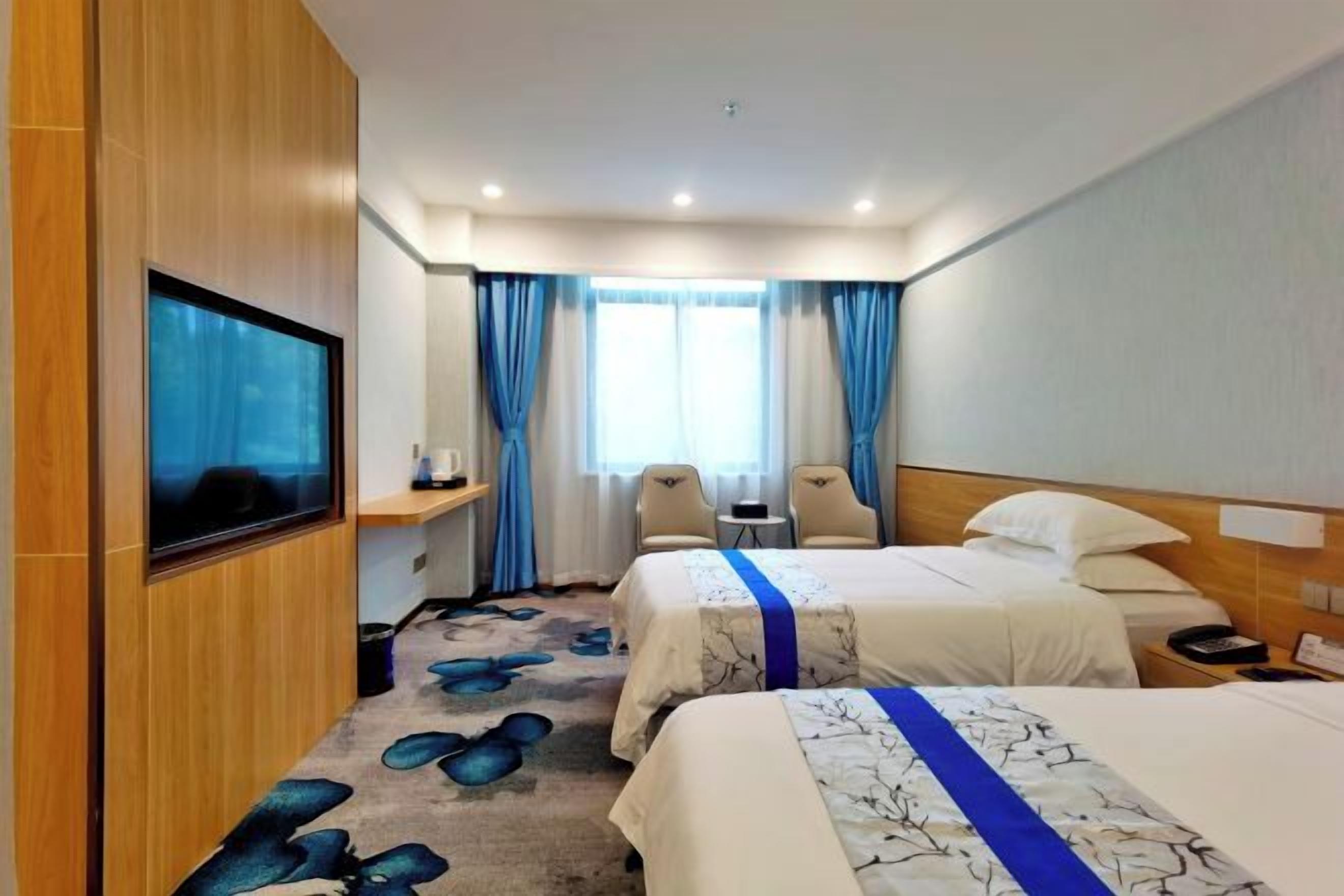 Ein Hotelzimmer mit zwei Betten, einem Fernseher, einem Schreibtisch und einem Sessel.