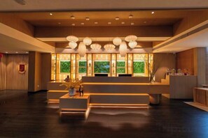 A reception area with a wooden reception desk, a seating area, and a large window with a view of greenery.