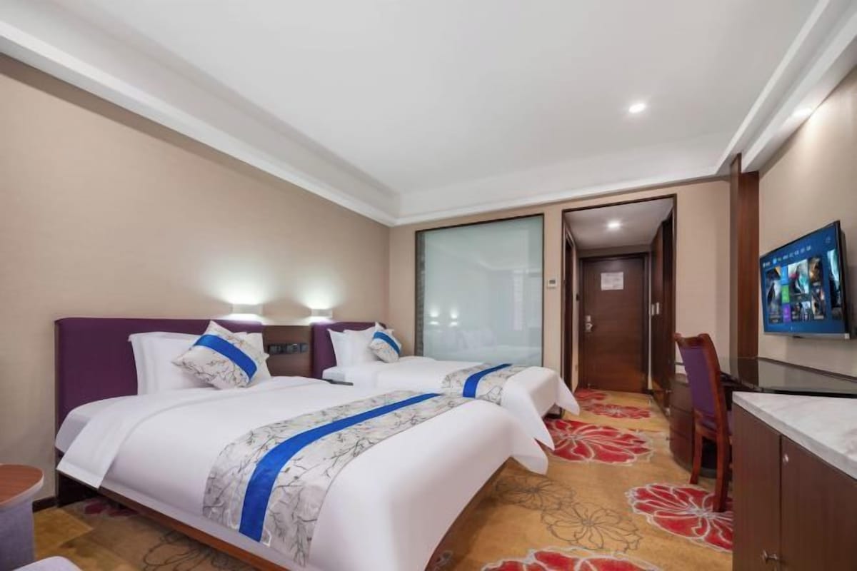 Habitación de hotel con dos camas, un televisor y piso alfombrado.