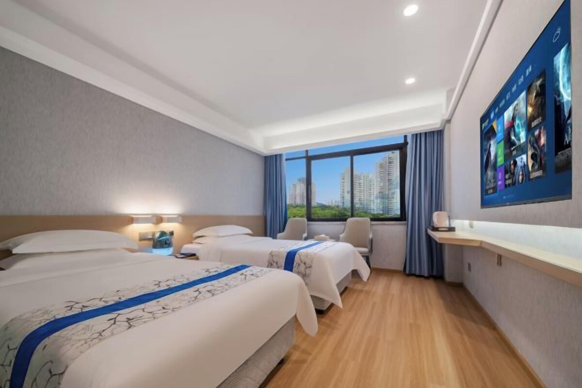 Habitación de hotel con dos camas, un escritorio, una silla y un ventanal con vistas a la ciudad.
