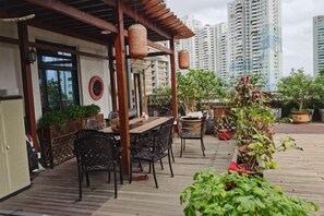 An outdoor patio with a wooden table and chairs, surrounded by potted plants and a pergola.