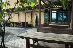 Un patio al aire libre con bancos y mesas de madera, una estructura de pérgola y vista al mar.