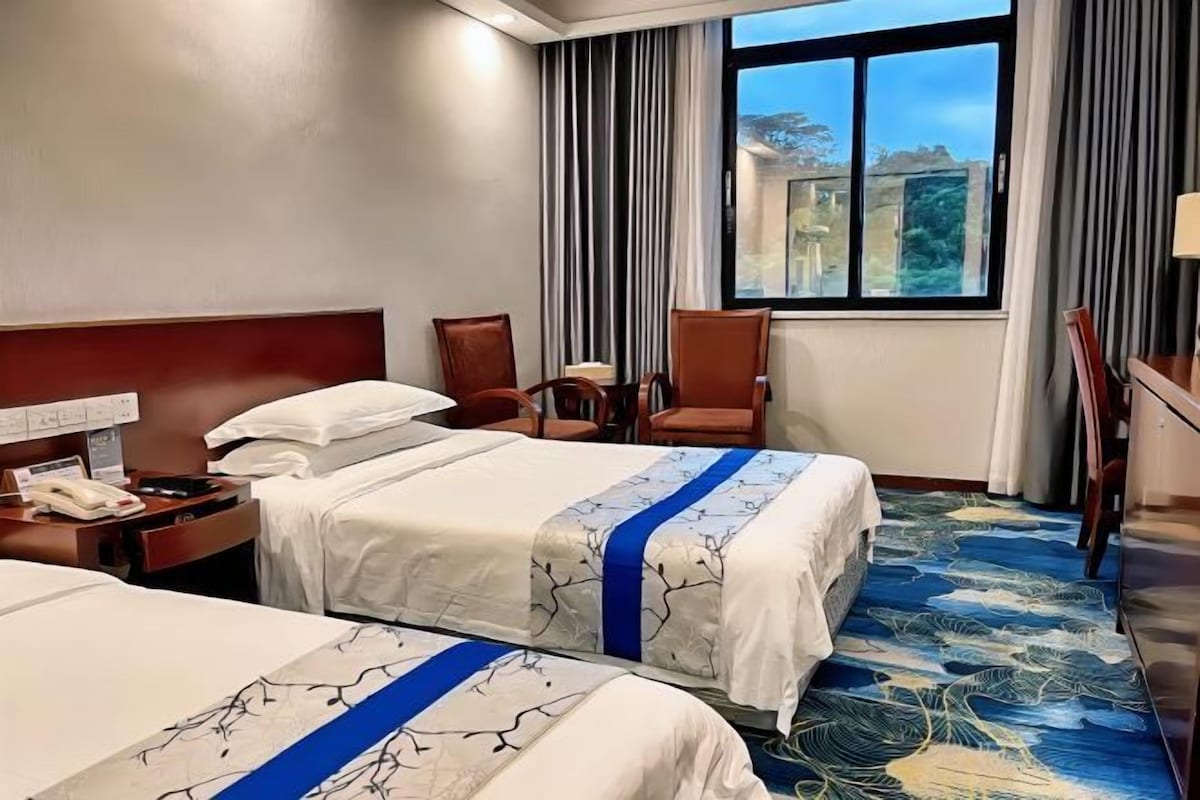 Habitación de hotel con dos camas, un escritorio con teléfono y una ventana con cortinas.