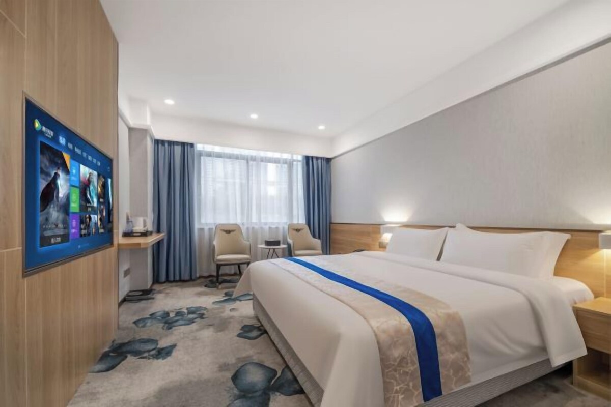 Una habitación de hotel con una cama grande, un escritorio, una silla, un televisor y una ventana con cortinas.