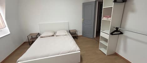 Een slaapkamer met een bed, een kledingkast en een deur naar een andere kamer.
