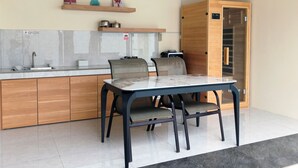 A modern kitchen with a dining area, wooden cabinets, a built-in oven, and a small shelf with decorative items.