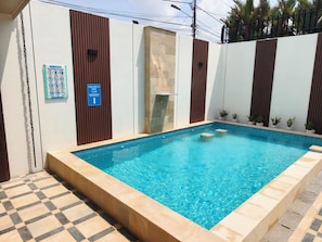 Una piscina con deck de azulejos, un cartel que indica la profundidad y una pared con listones de madera verticales.