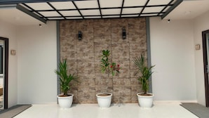 A modern building entrance with a stone facade, two potted plants, and a metal-framed awning.