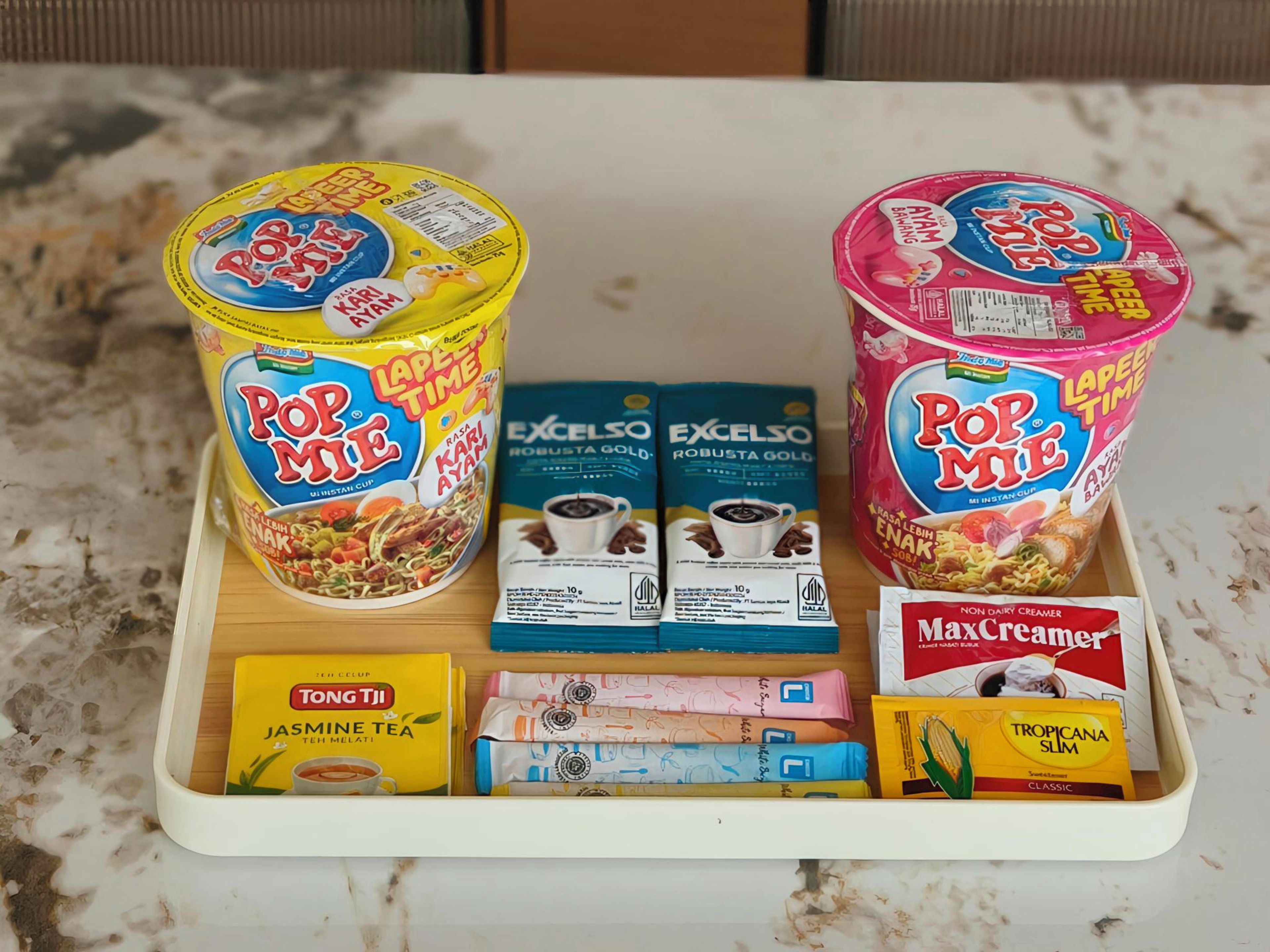 Una bandeja con fideos instantáneos Pop Mie, dos cajas de café Excelso, una caja de té jazmín Tong Tji, un paquete de leche condensada Max y un envase de jugo Tropicana Slim Classic.