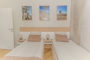 A double room with two beds, a wooden headboard, bedside tables with lamps, and three framed pictures on the wall. - Mediterranean Apartment in El Higuerón, Fuengirola – Your Peaceful Oasis (Fuengirola)