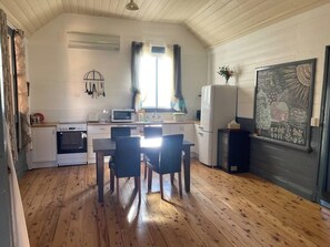 Kompakti keittiö, jossa on valkoiset kaapit, ruokapöytä tuoleineen, mikroaaltouuni, uuni ja jääkaappi.
