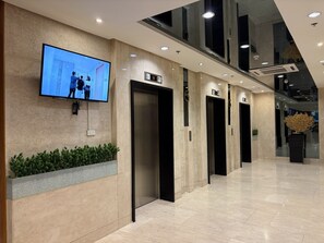 A modern elevator area with a flat-screen TV displaying a scene, multiple elevators, and a potted plant. - Modern & Fully Equipped Condo - near MOA Pasay with Washer-Dryer (Pasay City)