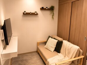 A modern living room with a sofa, a television, a wooden wardrobe, and wall-mounted shelves with plants. - Modern & Fully Equipped Condo - near MOA Pasay with Washer-Dryer (Pasay City)