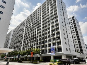 A multi-story building with a grid of balconies, a parking area with several cars, and a signboard with text. - Modern & Fully Equipped Condo - near MOA Pasay with Washer-Dryer (Pasay City)