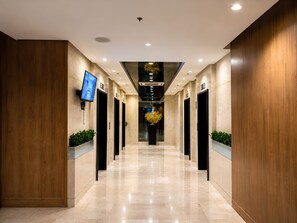 A modern hallway with multiple elevators, a flat-screen TV mounted on the wall, and potted plants. - Modern & Fully Equipped Condo - near MOA Pasay with Washer-Dryer (Pasay City)