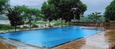 Una piscina rectangular con cerco de madera, rodeada de árboles y un cielo nublado.
