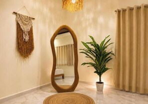 A room with a large mirror, a potted plant, a woven rug, and a curtain.