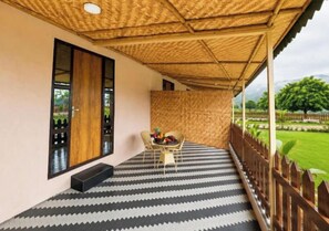 A covered outdoor seating area with a patterned floor, a table with chairs, and a view of a landscaped garden.