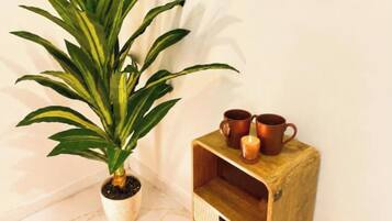 A potted plant, two copper mugs, and a candle on a wooden nightstand.